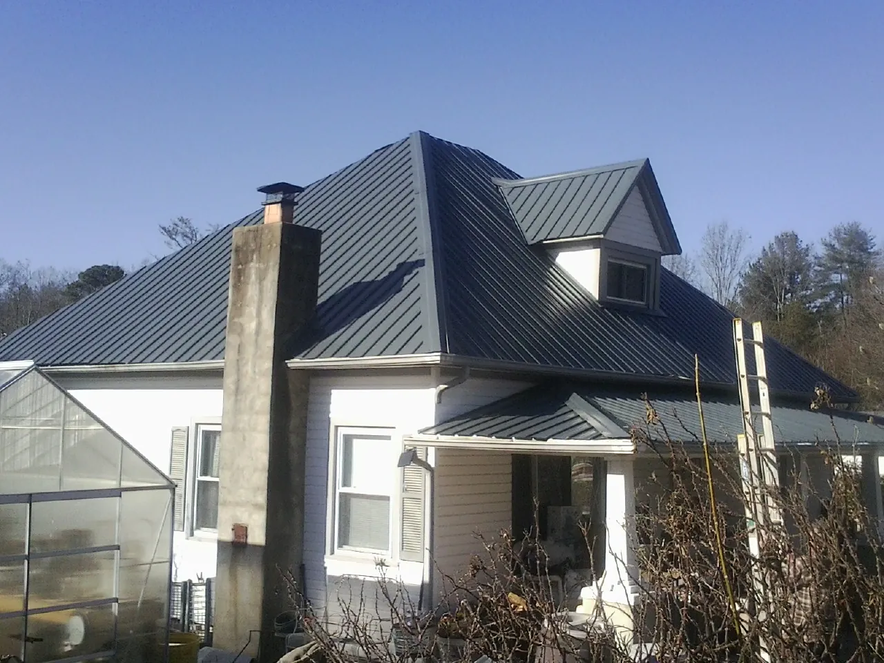 Dark blue standing seam metal roof on a white farmhouse with dormer — Slate & Tile Roof Repair by Roofing Brothers in Grand Valley