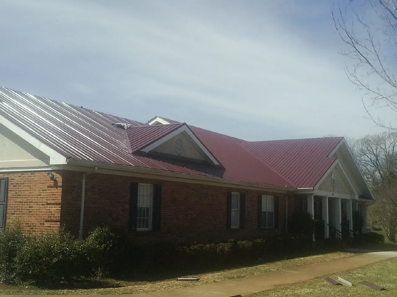 Red metal roof with gabled entries on a long brick building, from a Hail Damage Roof Repair job in Grand Valley