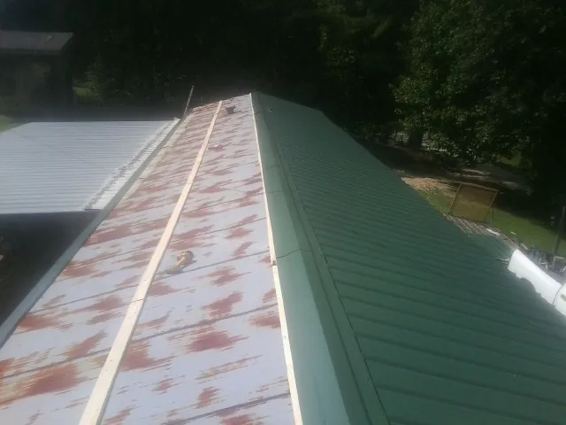 Old rusted panels beside newly installed green metal roofing — Wind Damage Roof Repair by Roofing Brothers in Grand Valley