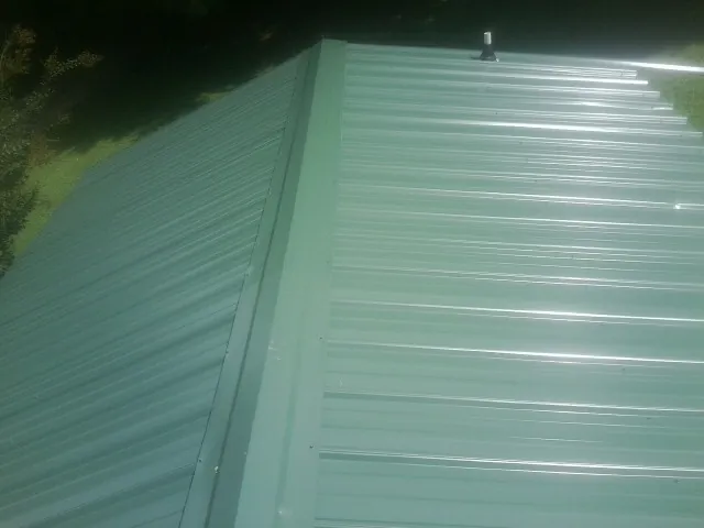 New green metal panels meeting at the ridge of a roof — Flat Roof Repair work by our crew in Grand Valley