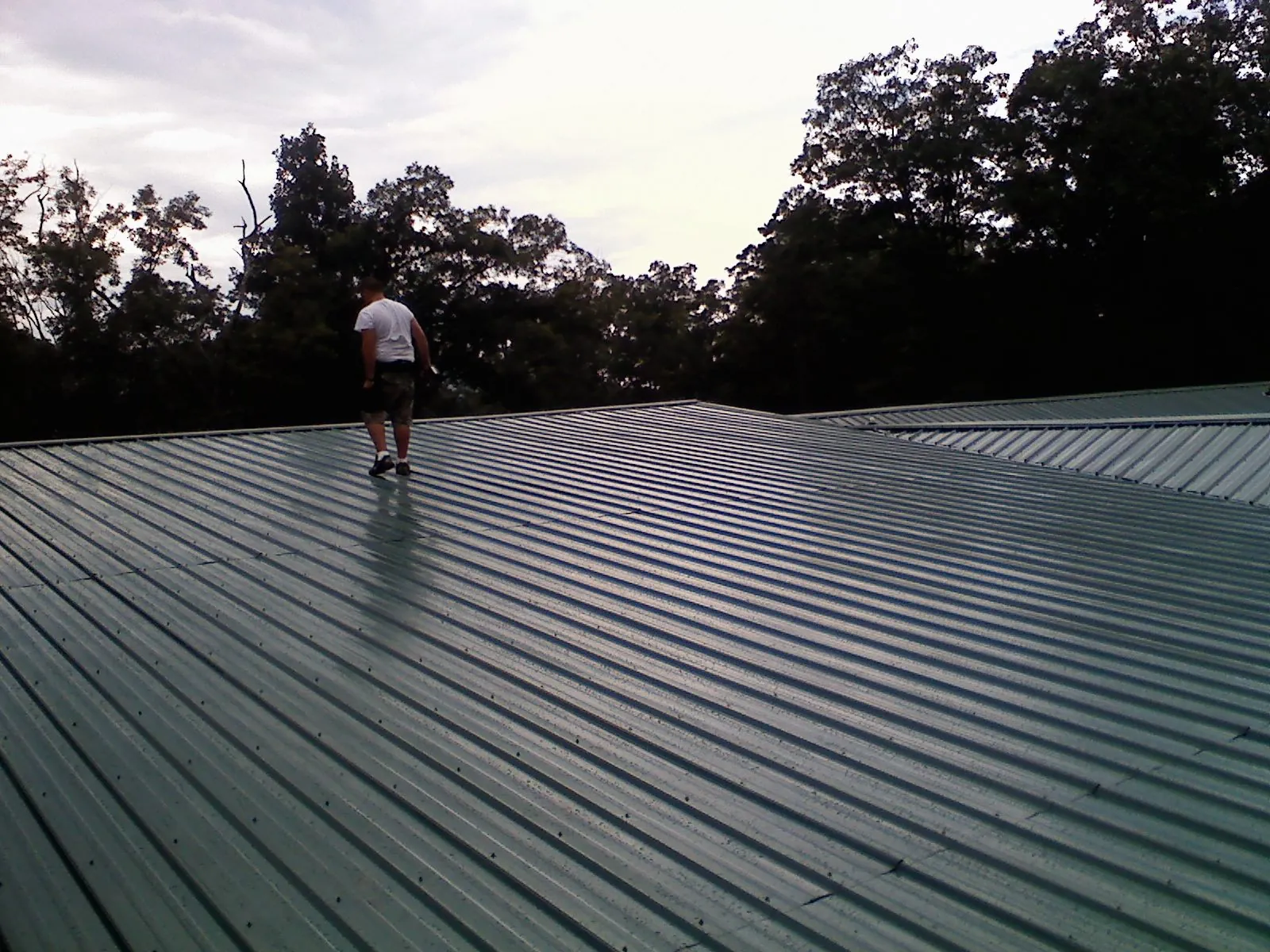 Roofer walking a wide expanse of new green metal roofing in Grand Valley