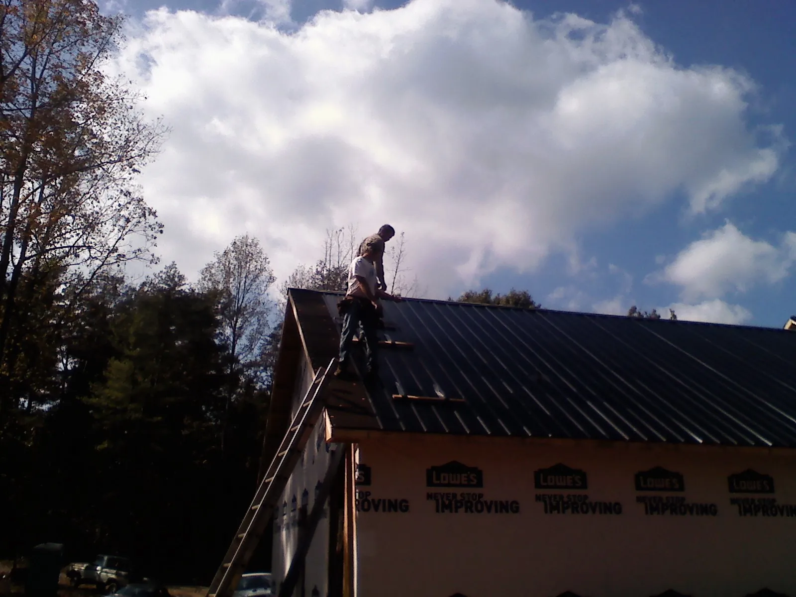 Roofer fastening dark metal panels high against a cloudy sky, from a Roof Inspection job in Grand Valley