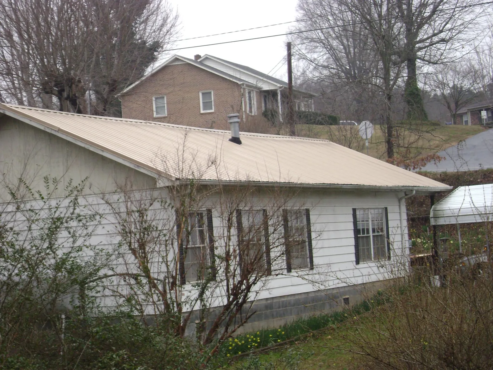 Tan metal roof on a white sided house set into a hillside — Commercial Roofing by Roofing Brothers in Grand Valley