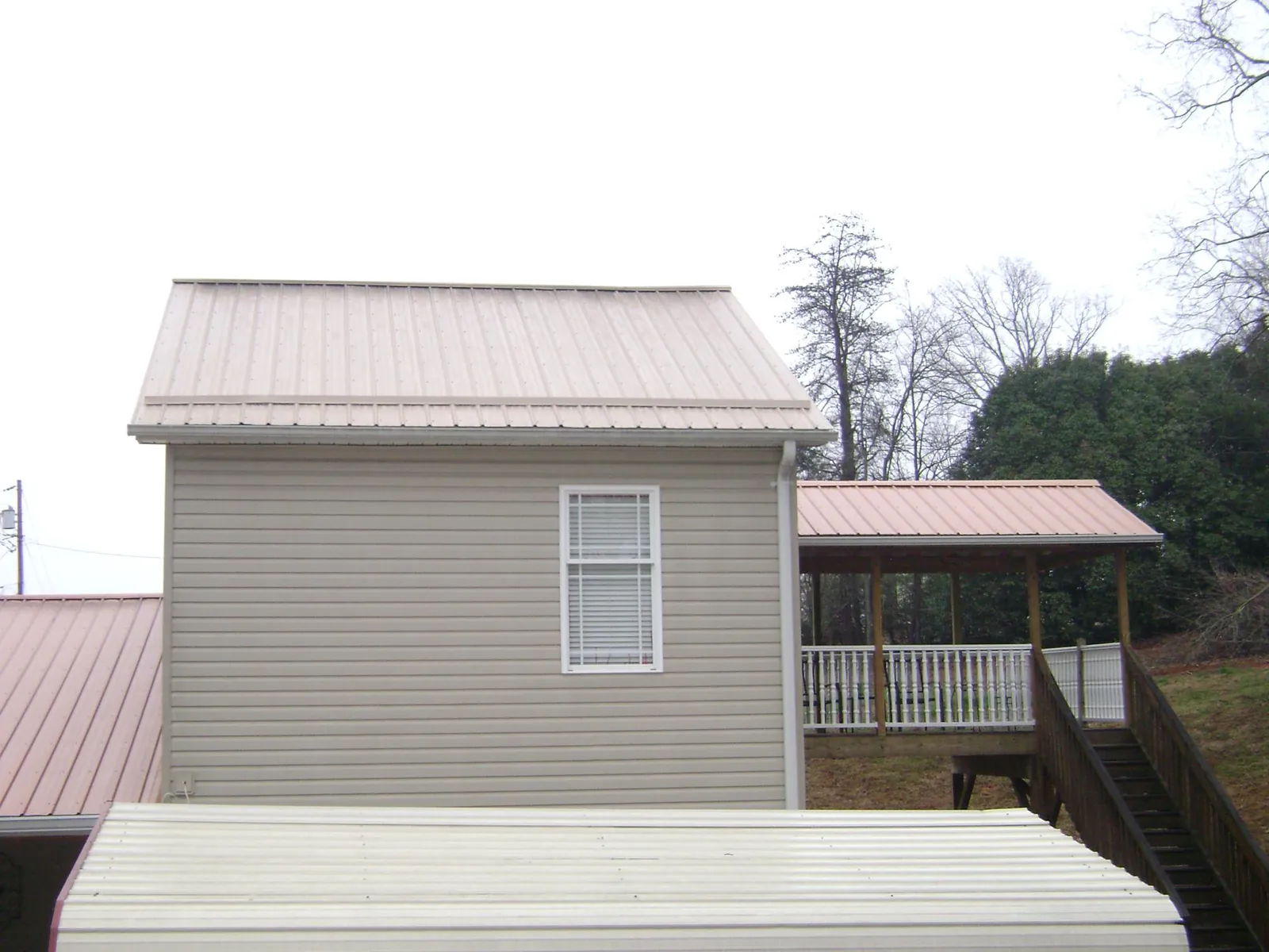 Tan metal roofs on a two story addition and attached porch, from a Roof Replacement job in Grand Valley